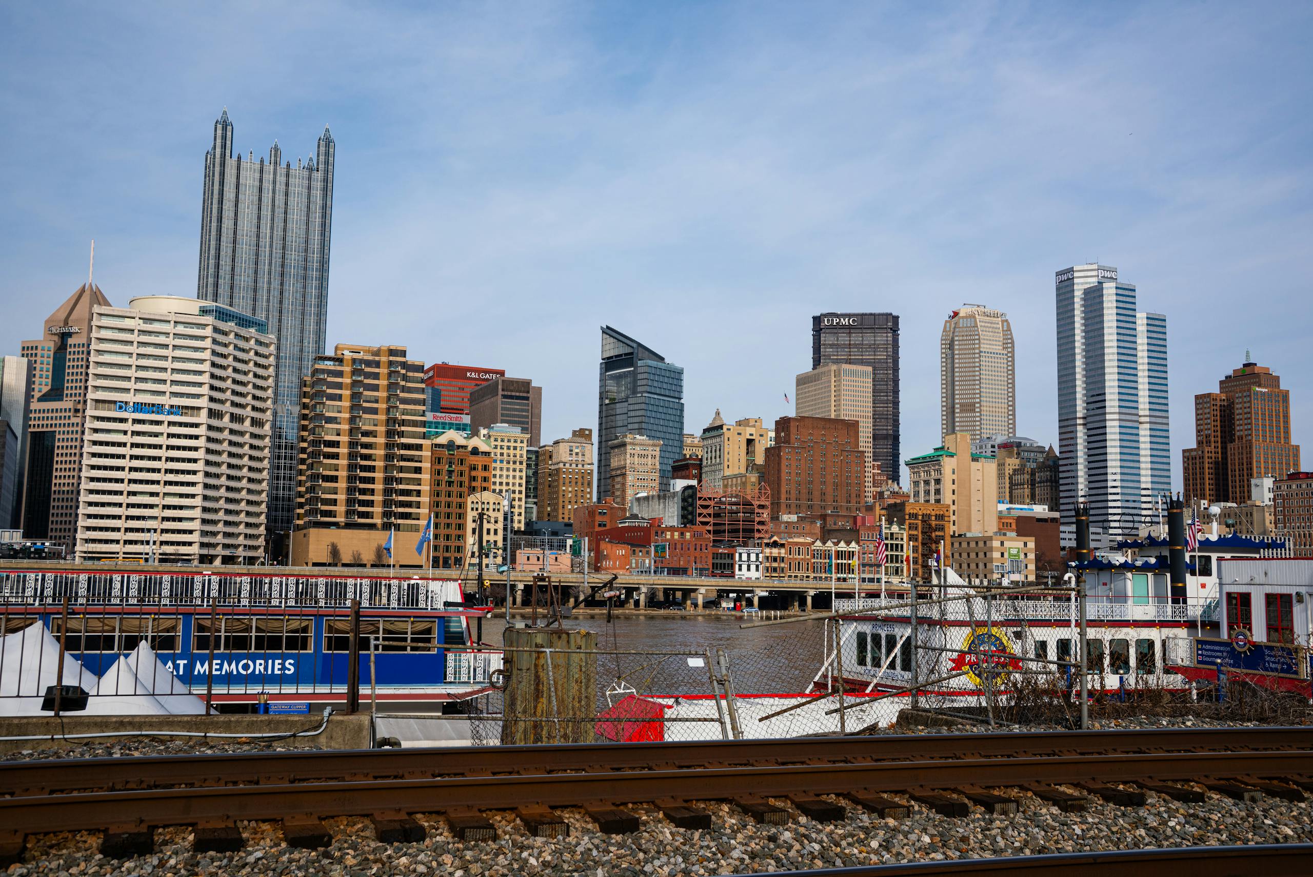 View of Pittsburgh skyline featuring prominent skyscrapers and a riverboat along the waterfront.